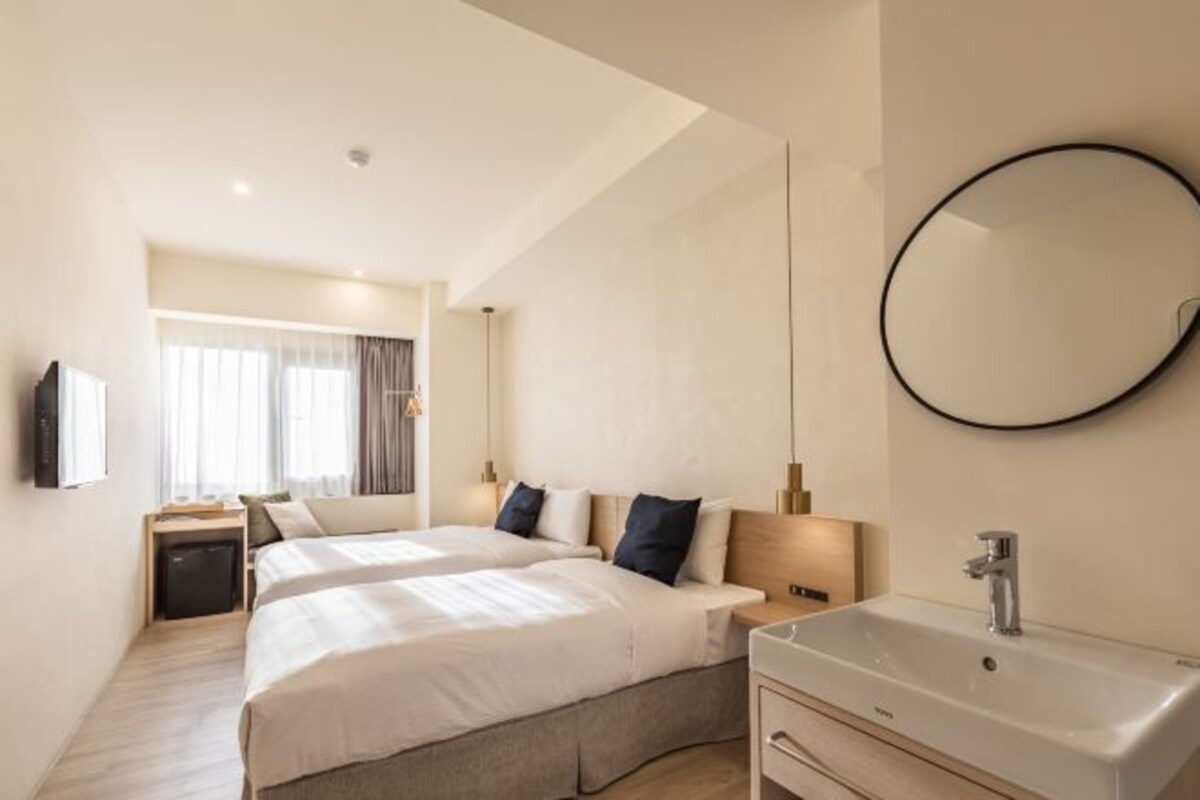Habitació d'hotel amb dos llits, un mirall gran, un lavabo i una televisió.