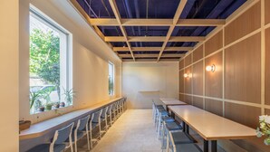 Ein modernes Interieur mit langen Tischen und Stühlen, großen Fenstern und einer Holzbalkendecke.