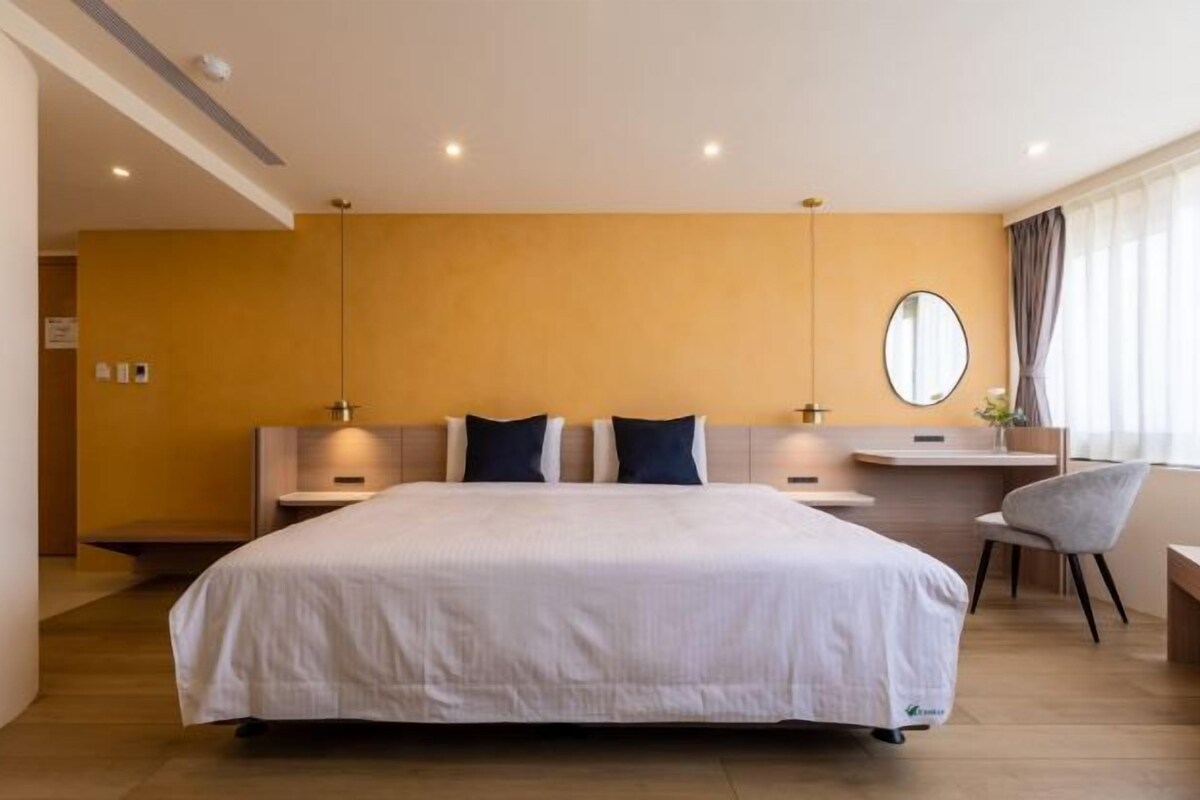 A modern hotel room with a large bed, bedside tables, a desk, and a chair.