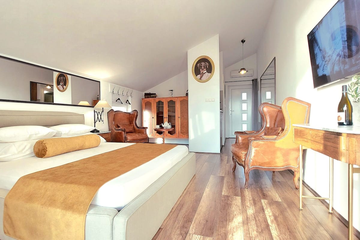 Un dormitorio moderno con una cama grande, suelo de madera, un escritorio con silla, televisión y armario.