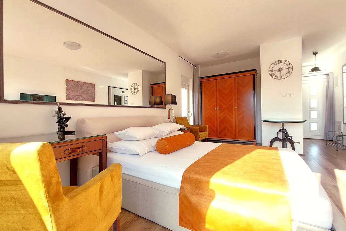 Habitación de hotel con una cama grande, un escritorio con lámpara, una silla, un armario y un espejo.