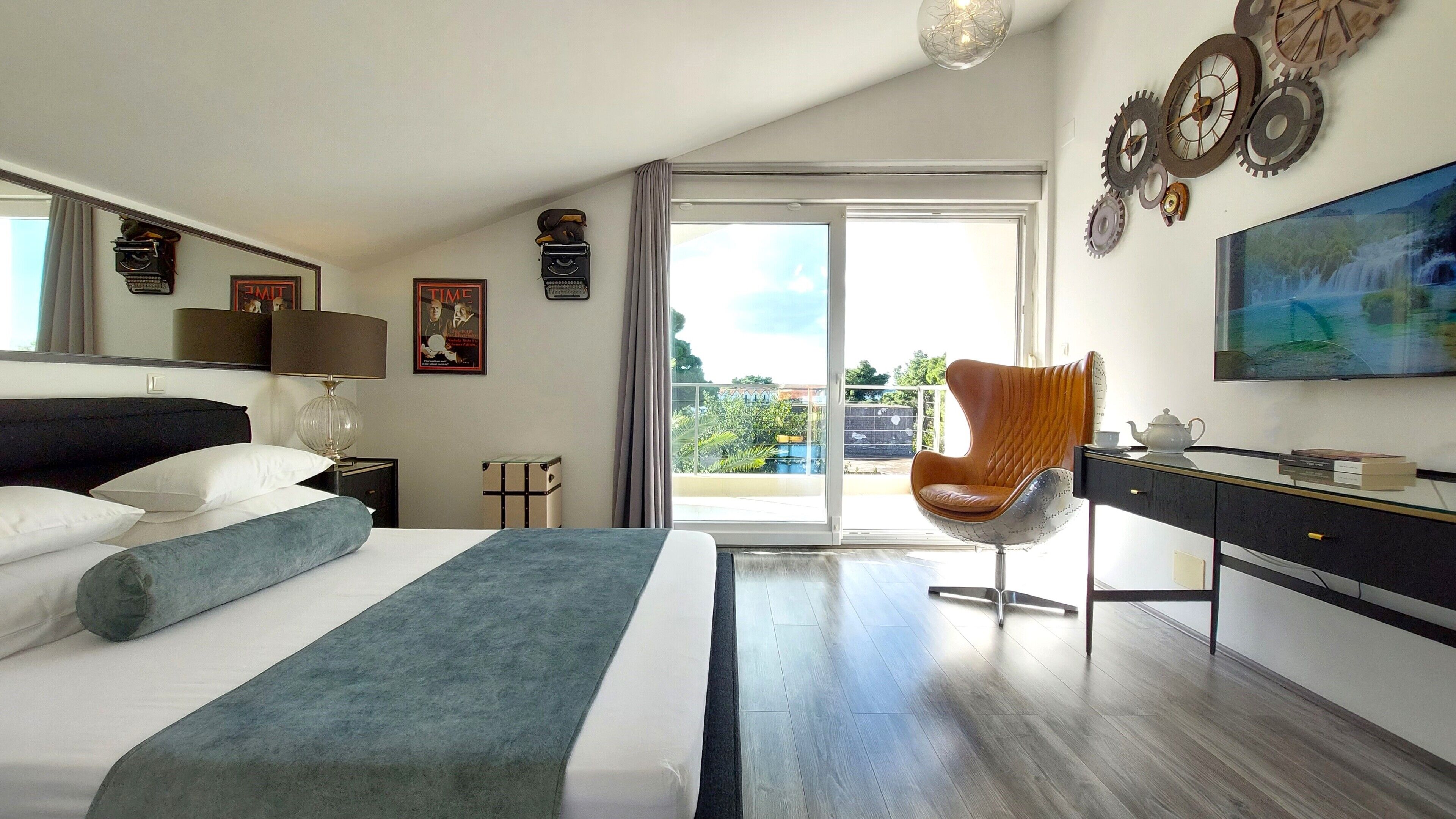 A hotel room with a bed, a chair, a desk, and a large window with a view of greenery.