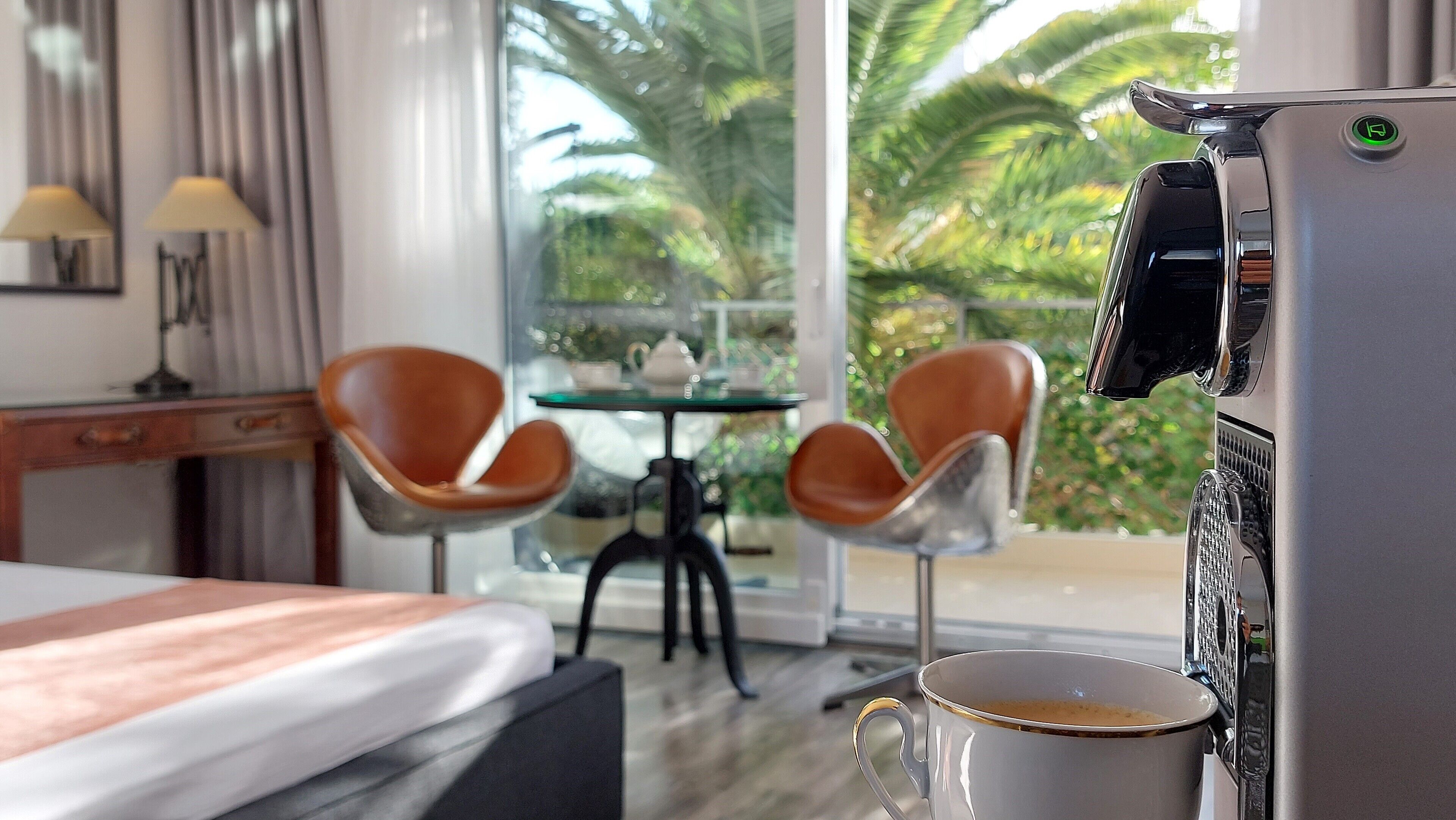 A hotel room with a bed, two brown leather chairs, a small table with a teapot, and a coffee machine.