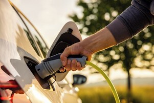 Una mano conectando un cargador para vehículo eléctrico a un coche.