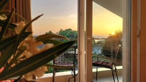 Un balcón con una silla y una mesa, con vista a un paisaje de árboles y una puesta de sol.