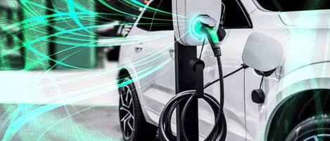 Un vehículo eléctrico blanco cargándose en una estación, con un enchufe iluminado.