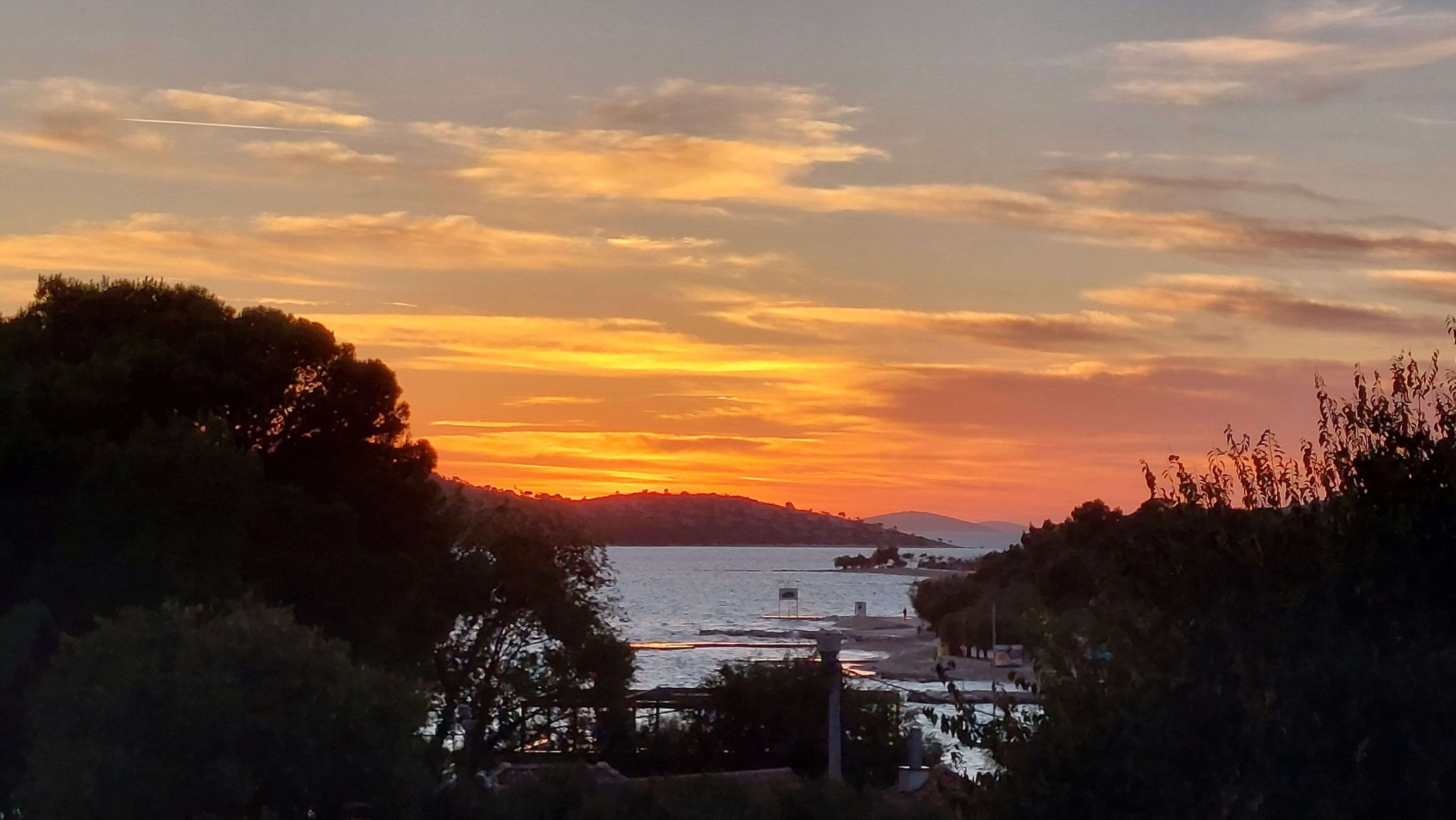 A sunset over a body of water with trees in the foreground.