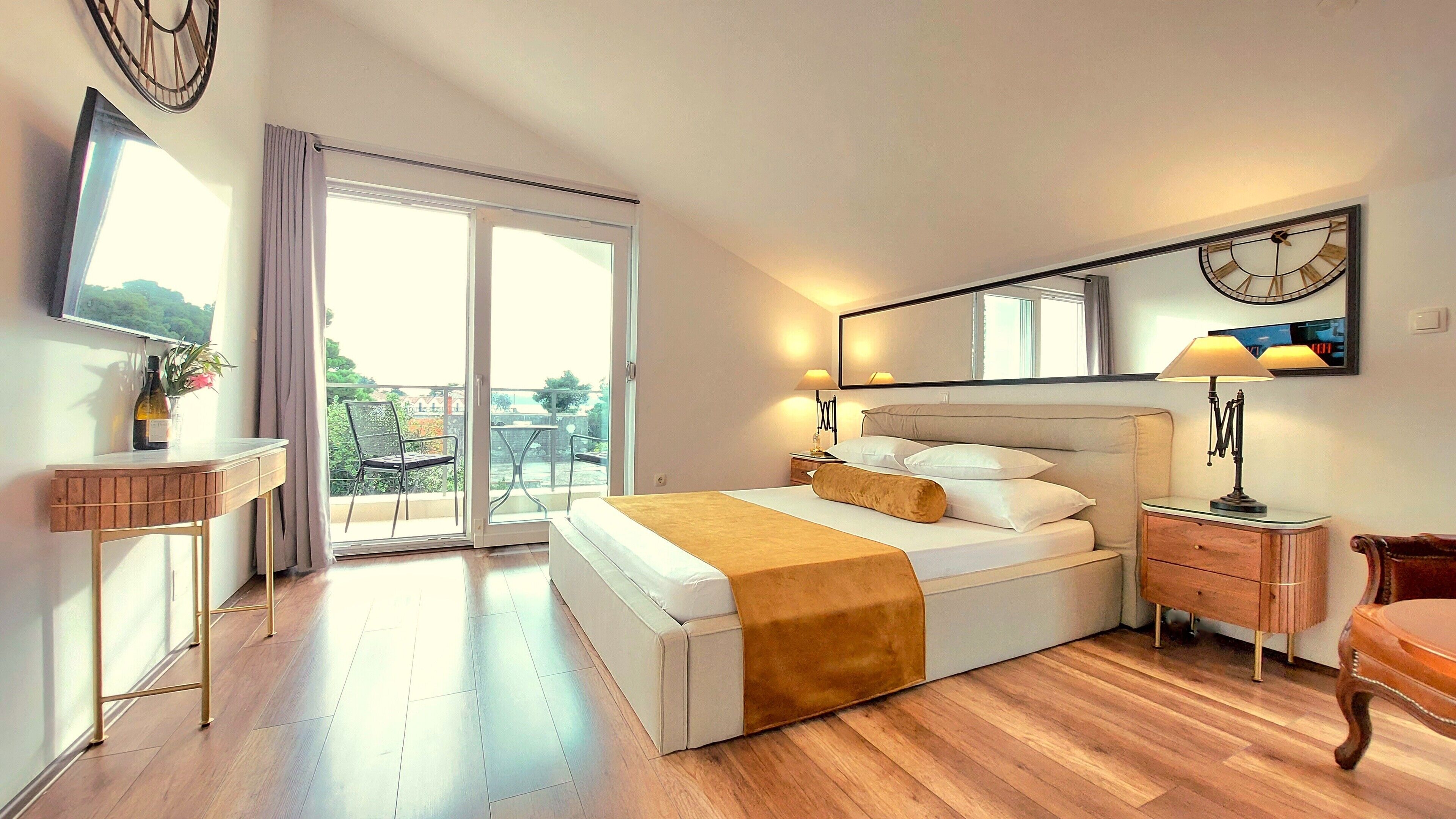 A hotel room with a bed, bedside table, lamp, and a large window with a view of the outdoors.