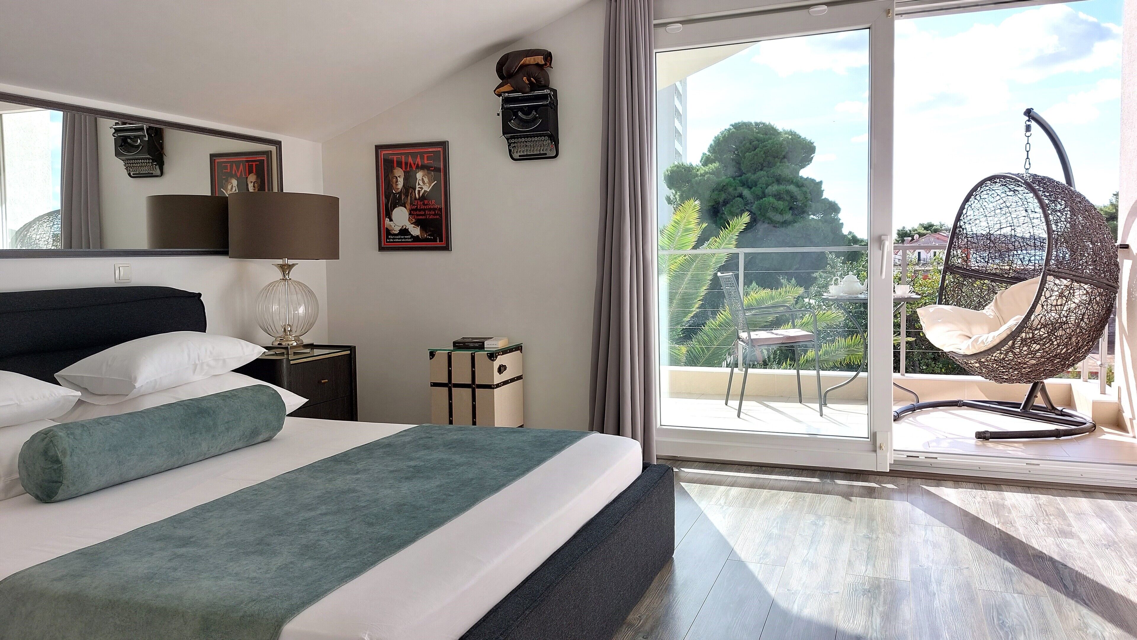 Hotelkamer met een bed, nachtkastje, lamp, stoel, balkon met hangstoel en uitzicht op groen.
