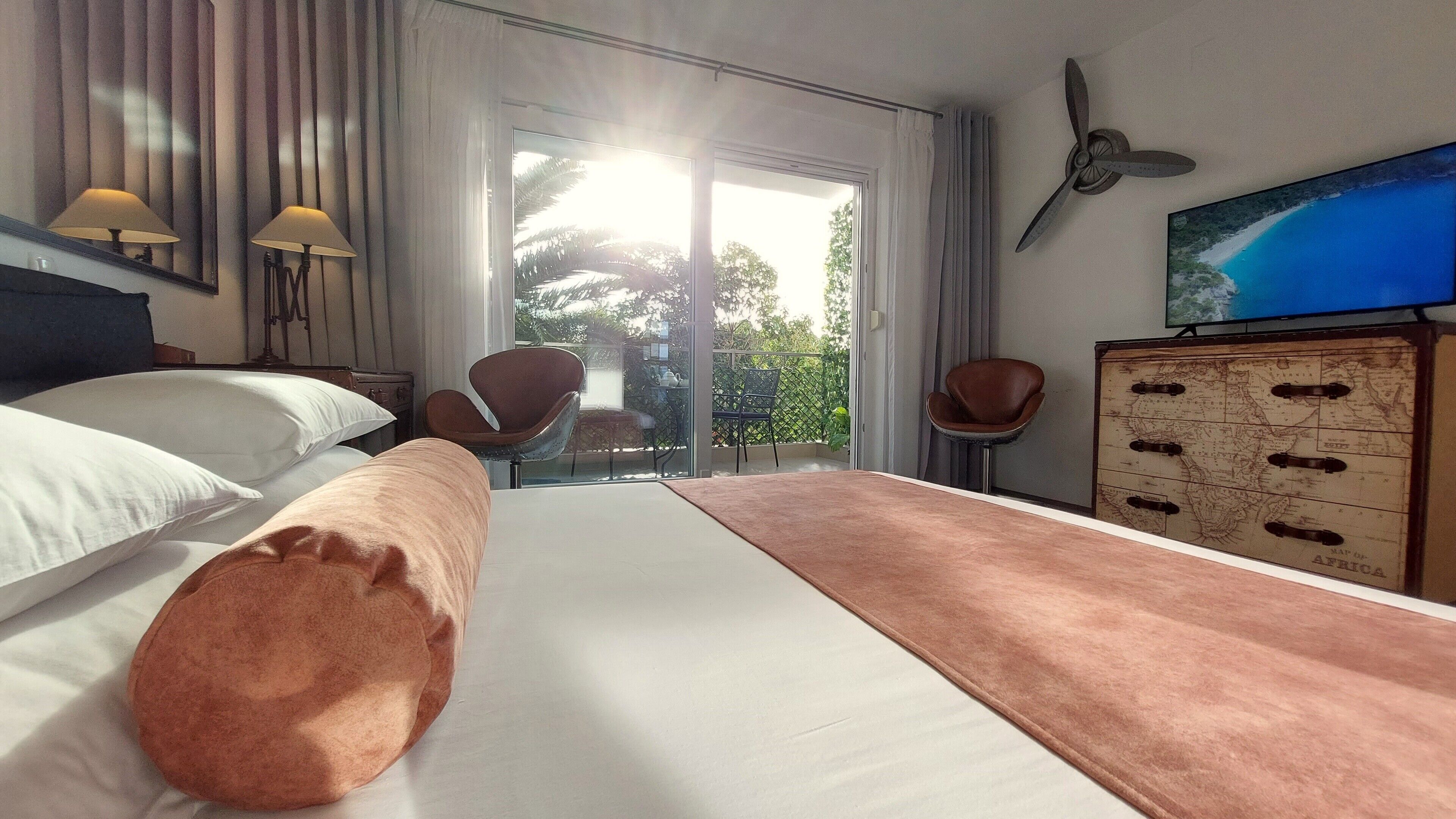A hotel room with a large bed, two chairs, a TV, and a dresser with a map.