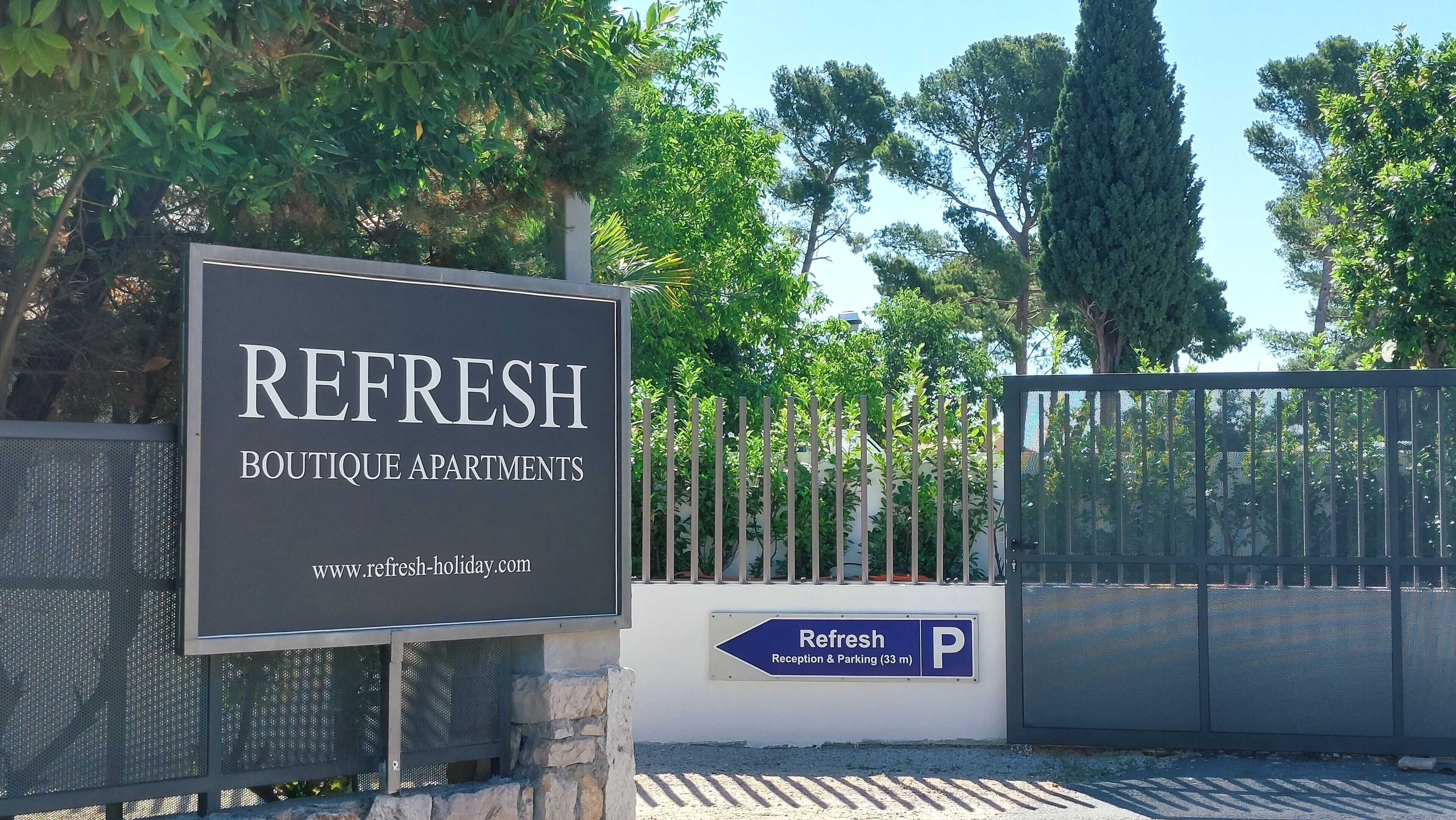 Une enseigne pour « REFRESH Boutique Apartments », avec l’adresse du site web et un panneau indiquant un espace de réception et de stationnement.