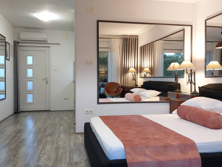 A hotel room with a large bed, a desk with a chair, a mirror, and a wardrobe.