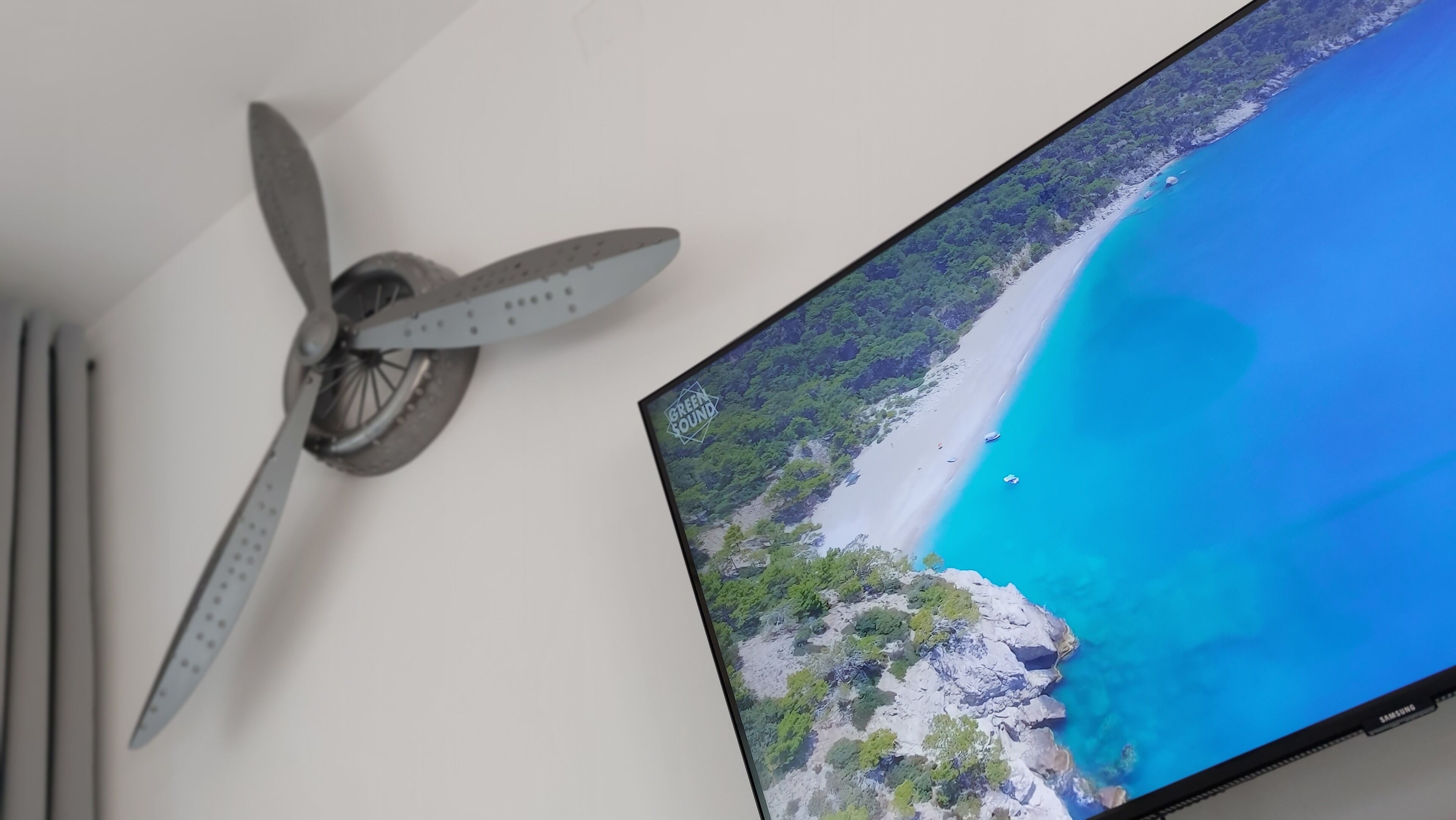 Un ventilador de techo y un televisor mostrando una escena de playa.