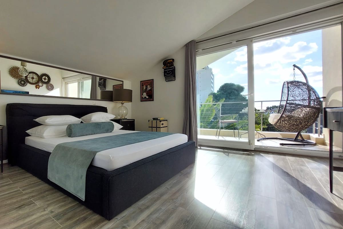 Un dormitorio moderno con una cama grande, una mesita de noche, una lámpara y vistas al exterior a través de un ventanal corredero.