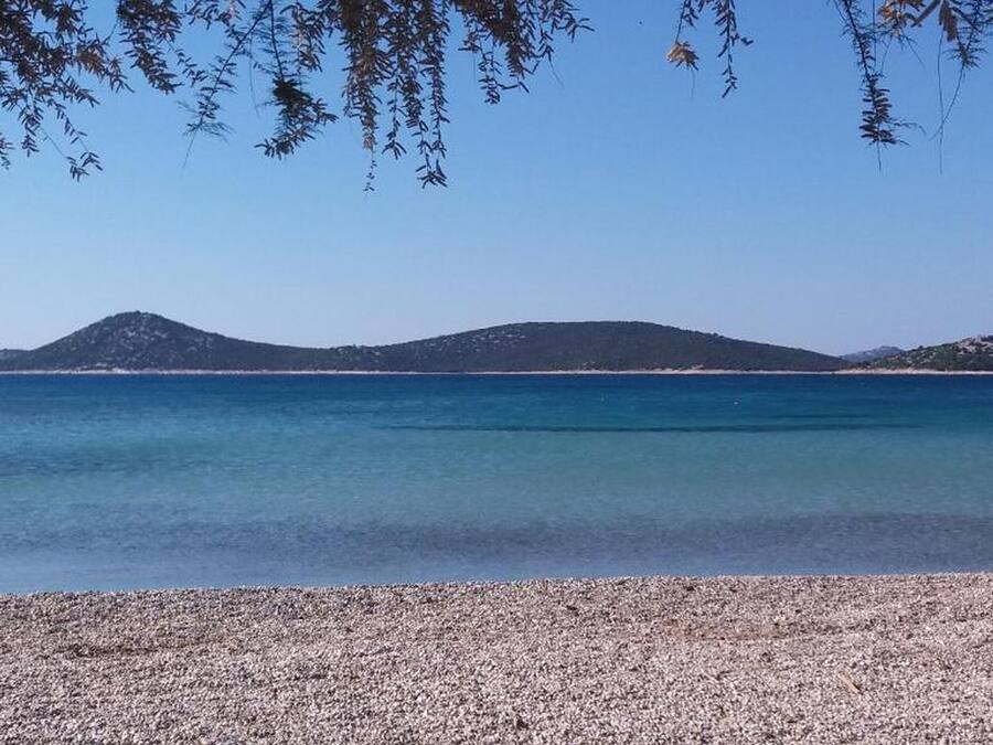Platja de petits còdols amb aigua turquesa cristal·lina i muntanyes allunyades.