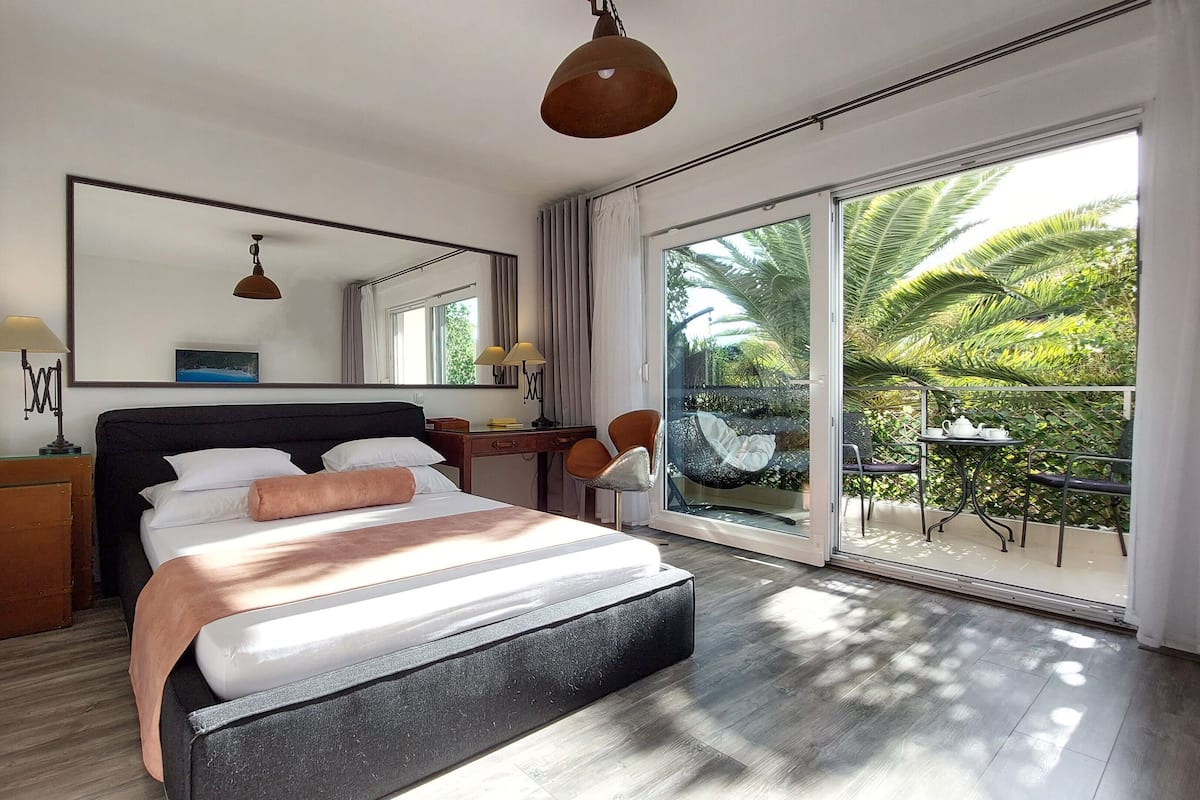 Habitación de hotel moderna con una cama grande, un escritorio y un balcón con vista a palmeras.