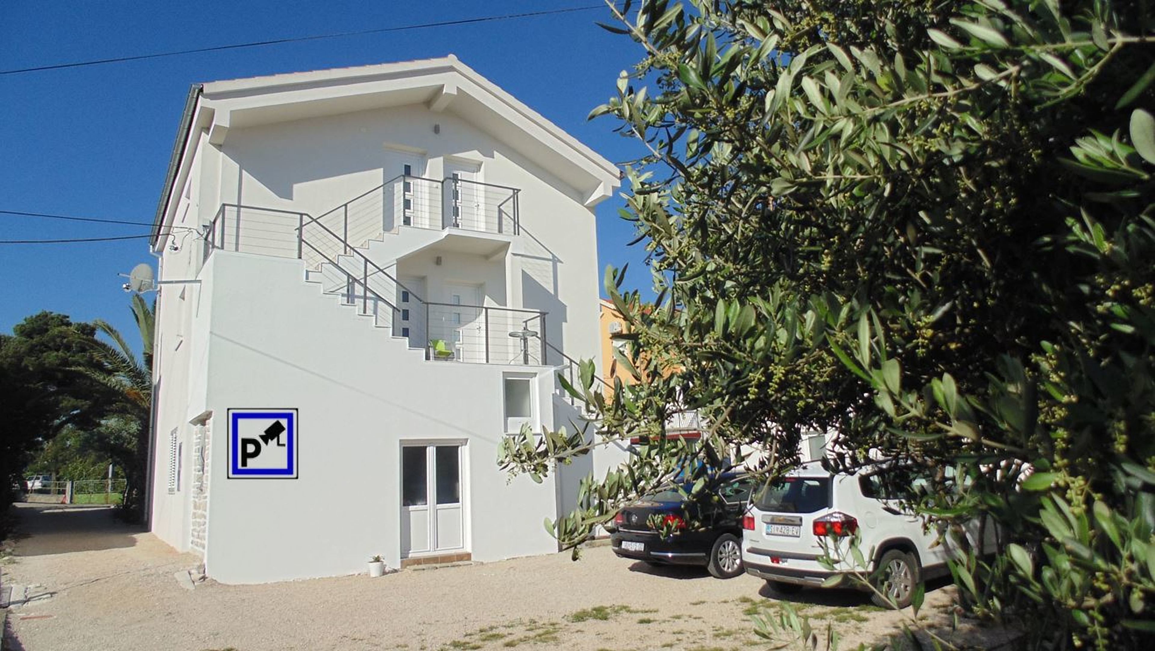 A two-story building with a white exterior, a visible staircase, and a parking sign indicating a parking area.
