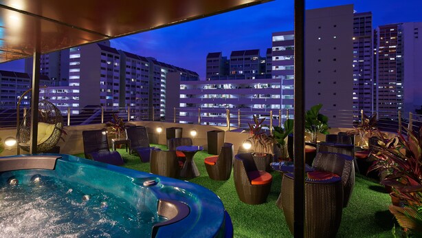 Een dakterras met een jacuzzi, rieten meubels en potplanten.