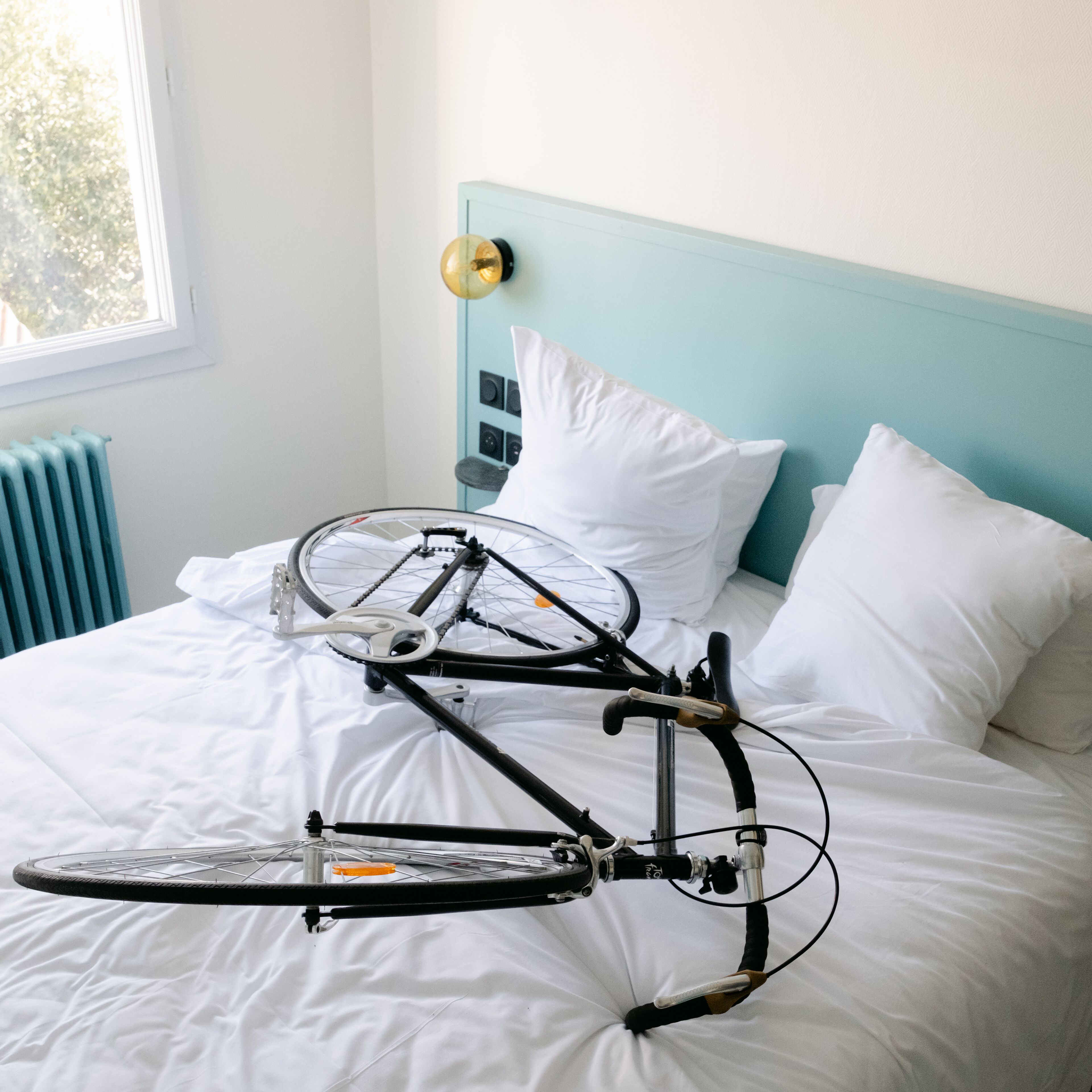 A bed with a bicycle placed on it, a window, and a radiator.
