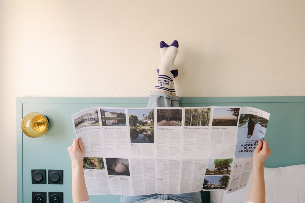 Una persona leyendo una revista con un títere de calcetín frente a una pared color turquesa.