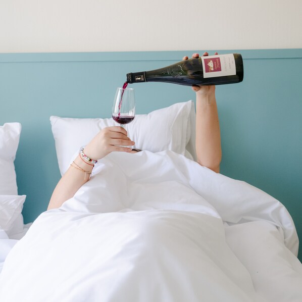 Una persona sirve vino en una copa mientras está acostada en la cama.