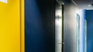 A hallway with a yellow wall on the left and a dark blue wall on the right, leading to a door marked '105'. - Le Lieu Dit (Nantes)