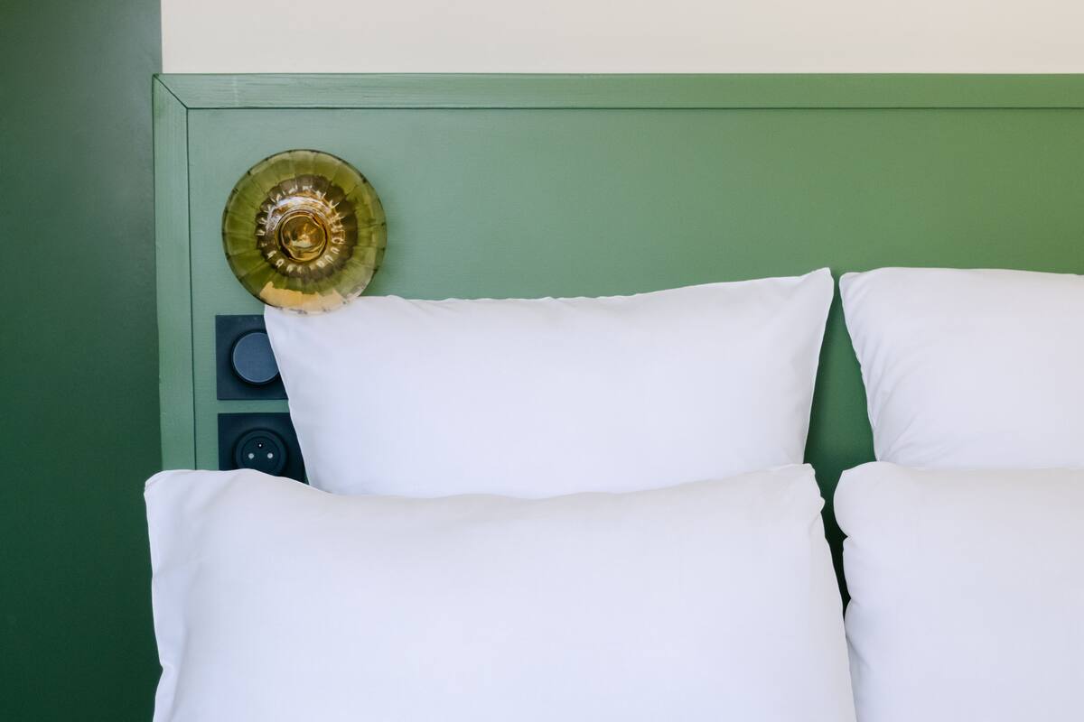 Una cama con almohadas blancas y un cabecero verde.