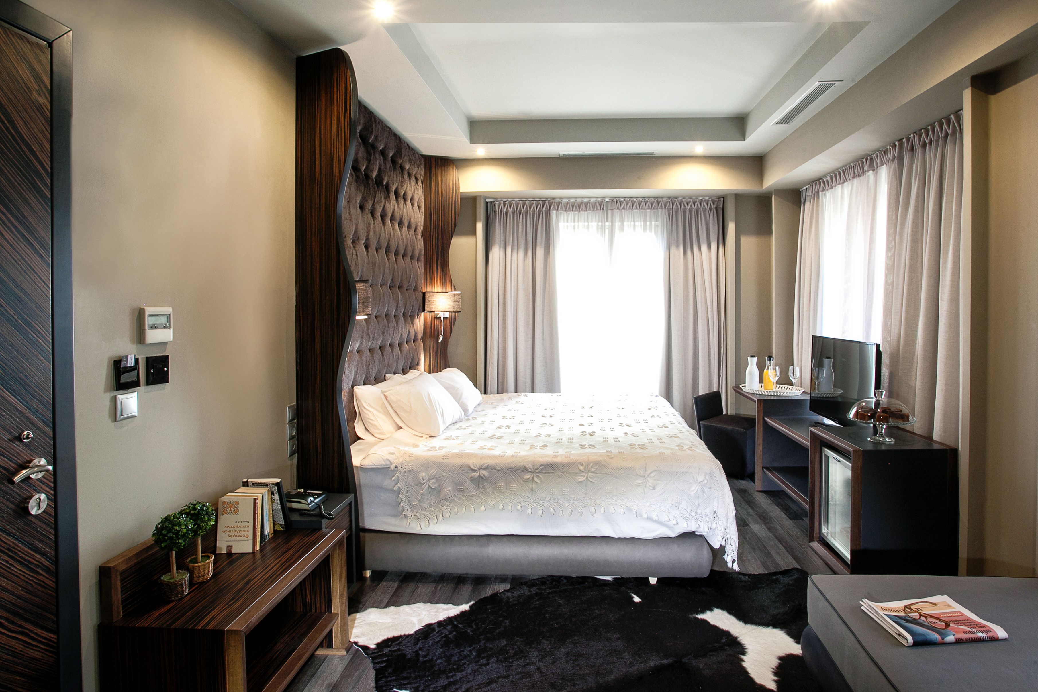 A modern hotel room with a large bed, a desk, a television, and a small seating area.