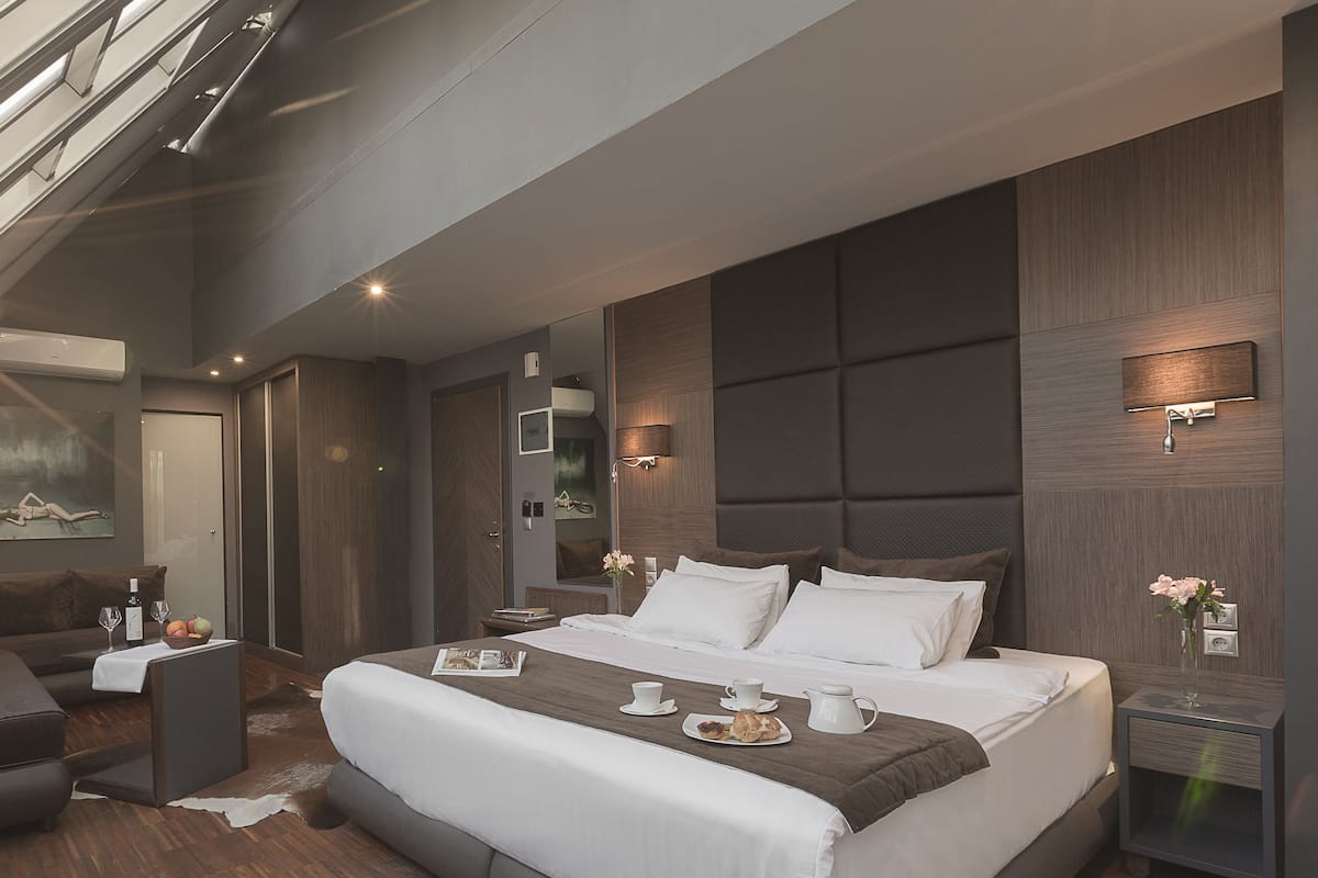 A modern hotel room with a large bed, a sofa, a small table with a vase of flowers, and a breakfast tray on the bed.