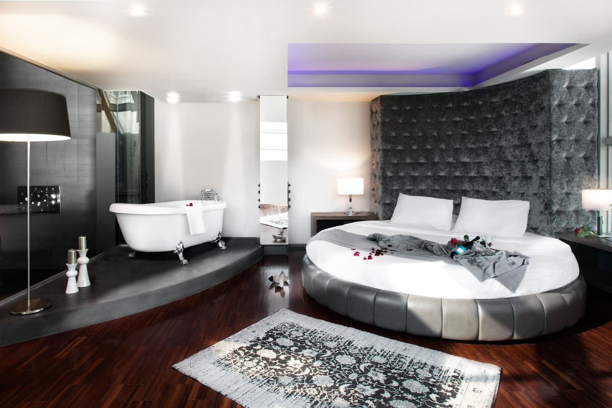 A modern bedroom with a round bed, a bathtub, and a stone accent wall.