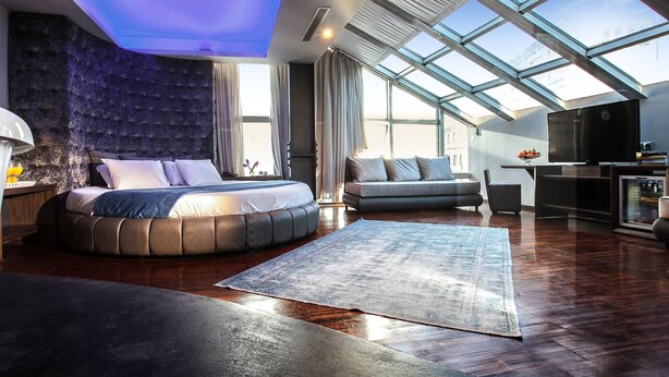 A modern bedroom with a skylight, a large bed, a sofa, and a TV. - Diamond Suites (Thessaloniki)