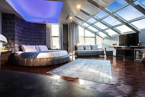 A modern bedroom with a skylight, a large bed, a sofa, and a TV. - Diamond Suites (Thessaloniki)