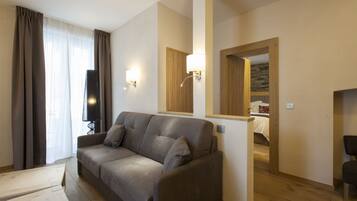 Una sala moderna con un sofá gris, piso de madera y un espejo que refleja un dormitorio.