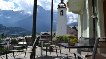 Una terraza con mesas y sillas, una torre de campanas y vistas a la montaña.