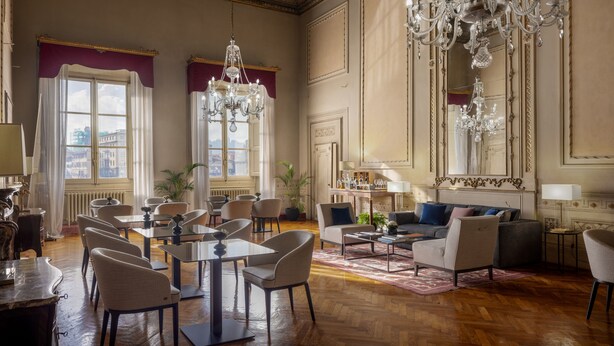 En rymlig hotellobby med högt i tak, utsmyckade kristallkronor och en sittgrupp med flera bord och stolar.