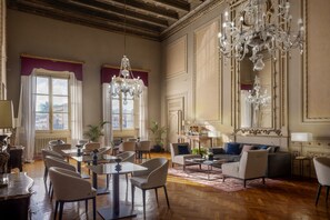 A spacious hotel lobby with a high ceiling, ornate chandeliers, and a seating area with multiple tables and chairs. - Leone Blu Suites | UNA Esperienze (Florence)