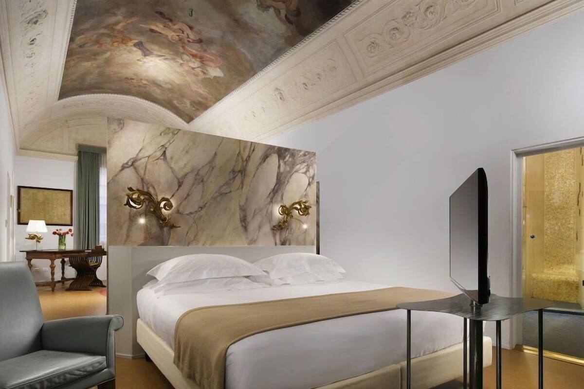 A hotel room with a bed, a television, a chair, and a marble wall.