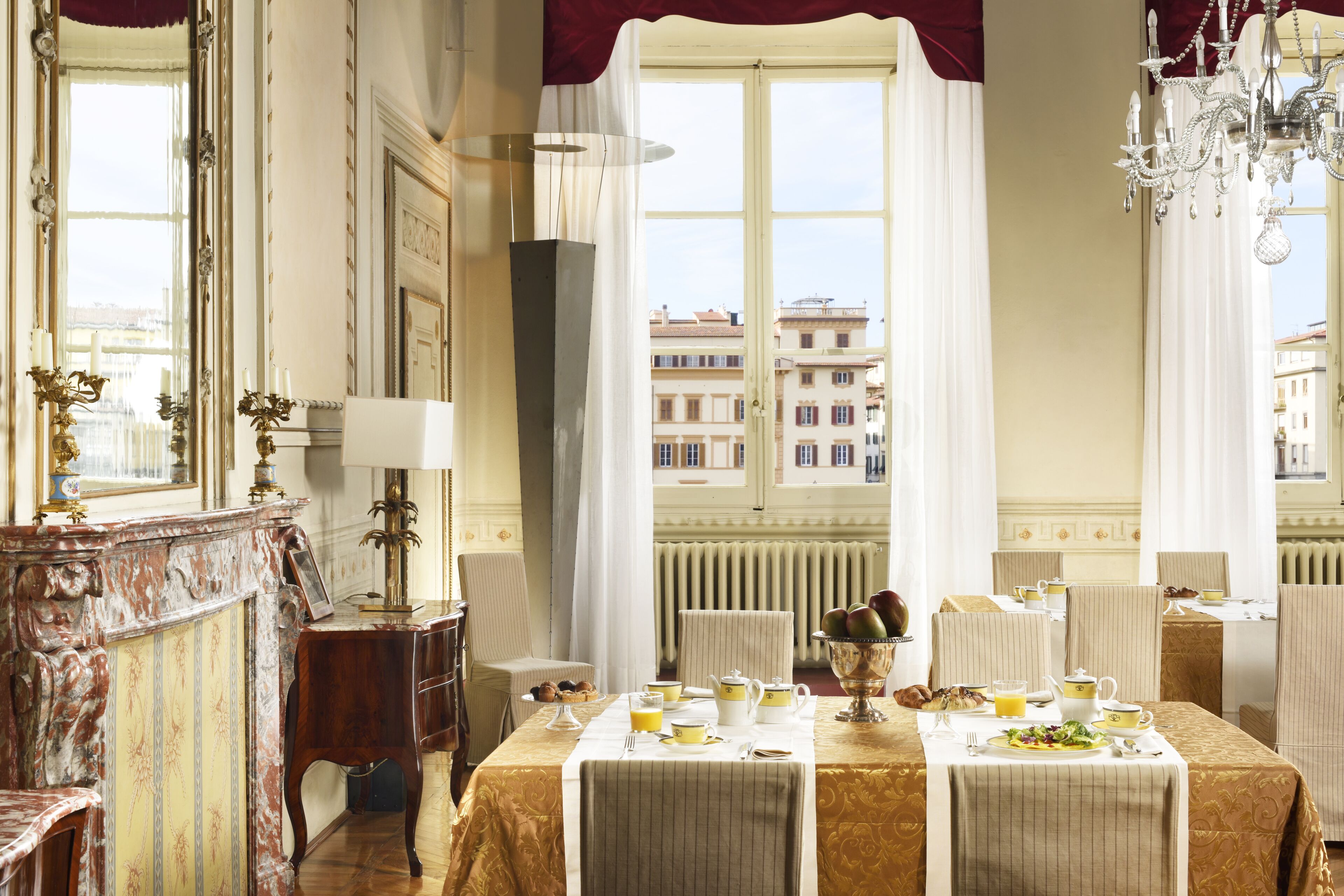 A dining room with a table set for breakfast, a chandelier, and a view of buildings outside.