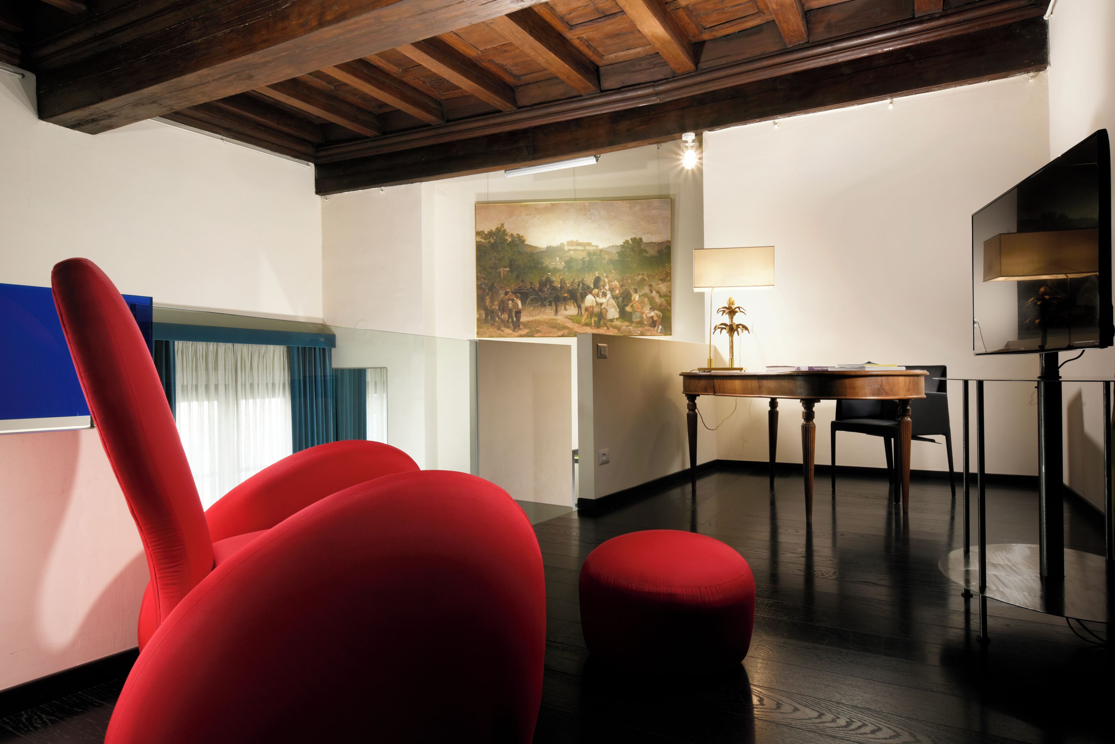 A room with a wooden ceiling, a painting on the wall, a table with chairs, and a red chair.