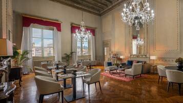 A spacious hotel lobby with high ceilings, chandeliers, and a view of the city through large windows.