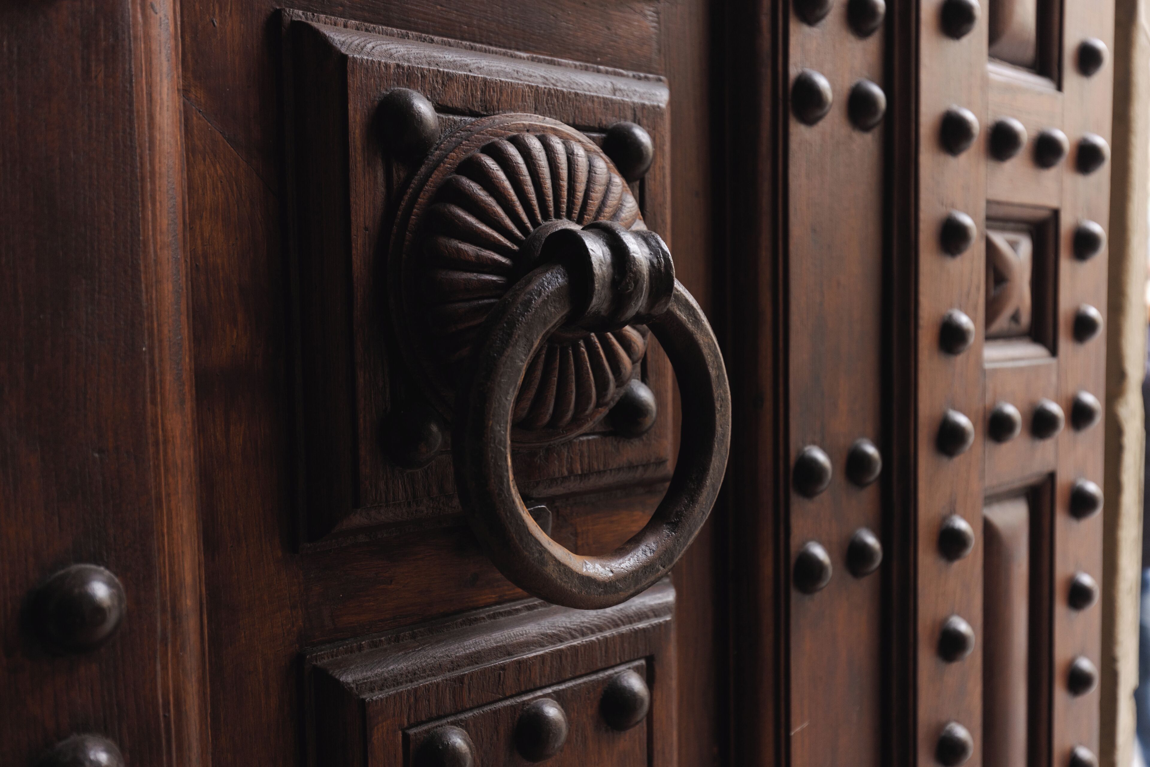 A wooden door with a decorative knocker and a series of round knobs.