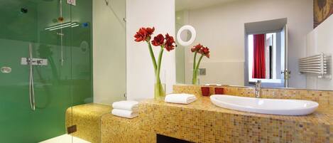 A modern bathroom with a glass shower enclosure, a large sink with a mirror, and decorative red flowers.