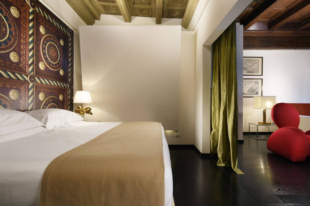 A hotel room with a large bed, a wooden ceiling, a green curtain, and a red chair.