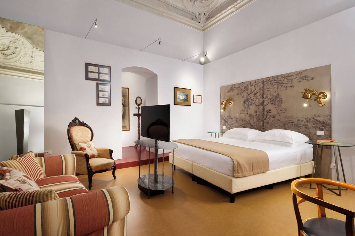 A hotel room with a large bed, a TV, a sofa, a chair, and a desk.