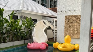 En swimmingpool med krystalklart, blåt vand, omgivet af græs og beplantning. Oppustelige vandrutsjebaner og ringe i pink og gul.