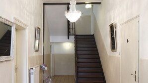 A hallway with a patterned carpet, a chandelier, a staircase, and a door with a number. - Hotel Am Lindenhof (Hannover)
