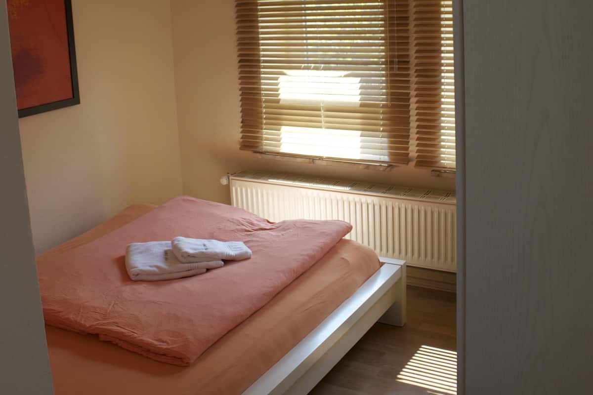 A bedroom with a single bed, a radiator, and a window with blinds.