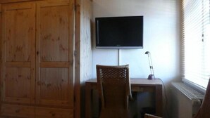 A room with a wooden wardrobe, a desk with a computer, a television mounted on the wall, and a window with blinds. - Hotel Am Lindenhof (Hannover)
