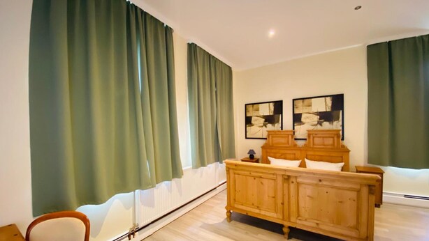 A bedroom with a wooden bed, green curtains, a white radiator, and two abstract paintings on the wall. - Hotel Am Lindenhof (Hannover)