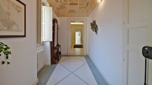 A hallway with a tiled floor, a map on the wall, a radiator, and a door with a safety device. - Palazzo Rollo (Lecce)